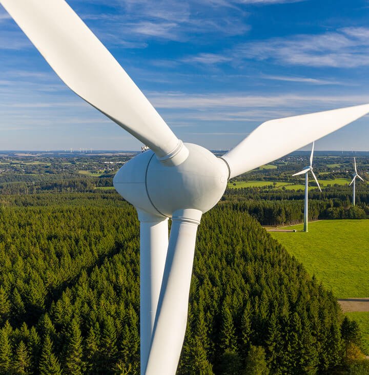 wind power turbine above forest with blue skies